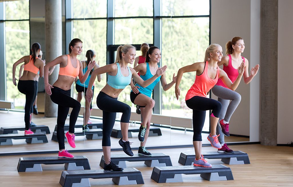 fitness, sport, training, gym and lifestyle concept - group of women working out with steppers in gym